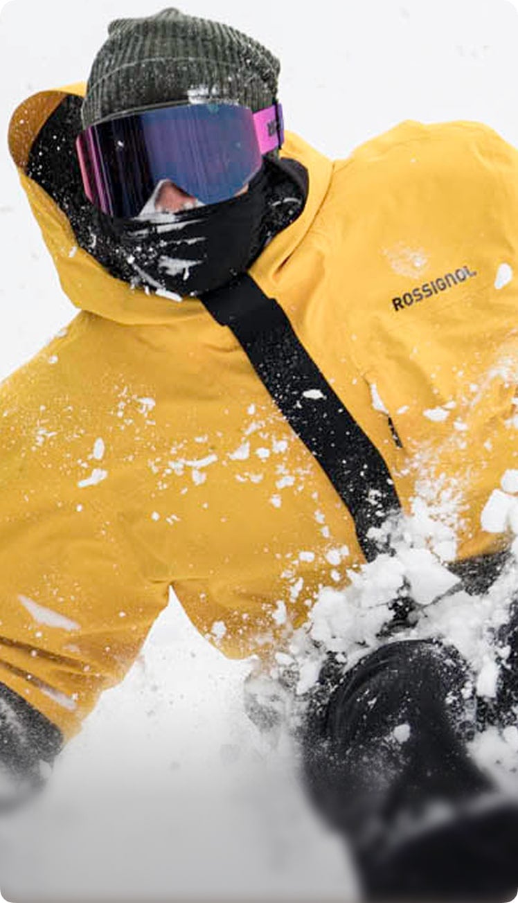 Sciatore che avanza nella neve fresca, con una giacca gialla Desafio 2L e una maschera Otava viola.