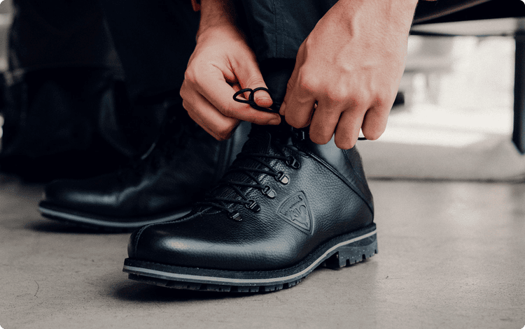 Nahaufnahme von Händen, die die Schnürsenkel eines schwarzen Rossignol-Stiefelpaars festziehen.