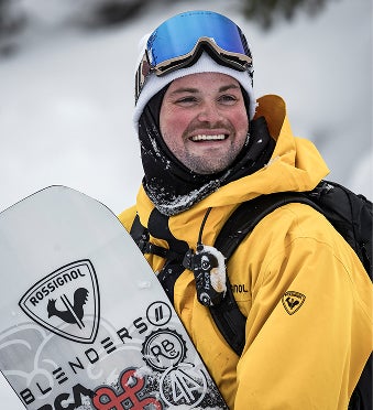 Smiling snowboarder holding a Rossignol snowboard, proudly displaying the logo