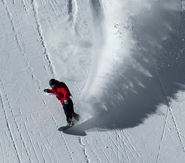 Snowboarder seen from above making a fast carve on a mountain piste, riding a Rossignol snowboard at high speed