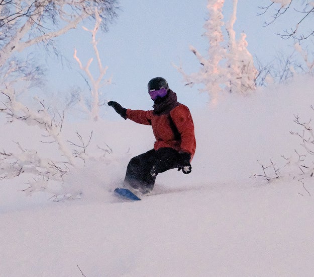 Relaxed snowboarder riding through trees in a forest on a Rossignol snowboard