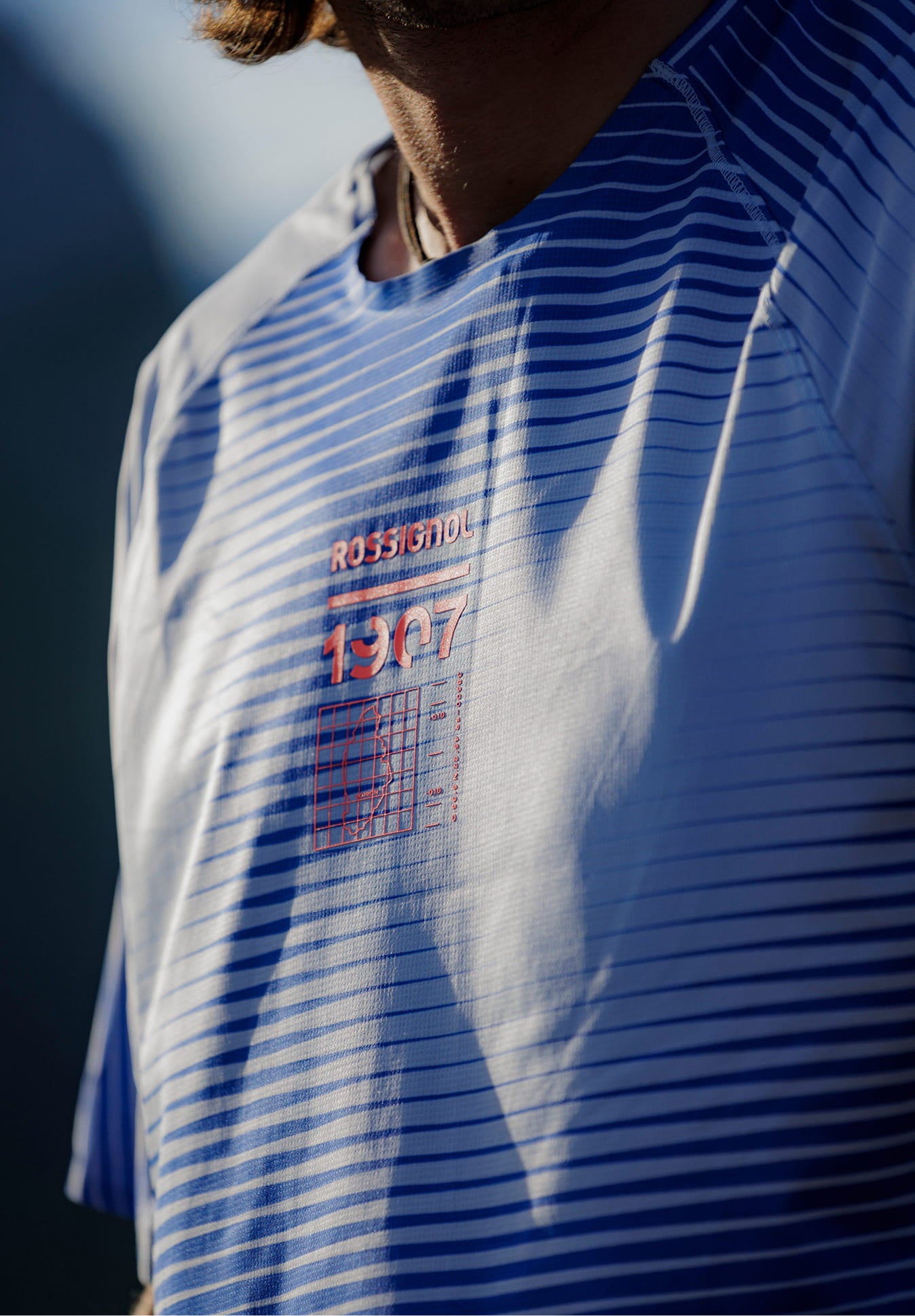 Close-up of the front of a blue Rossignol technical T-shirt with horizontal line patterns.