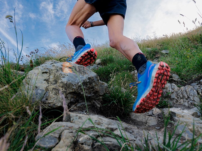 Une personne court sur un sentier rocheux en montagne, vue rapprochée sur les chaussures.