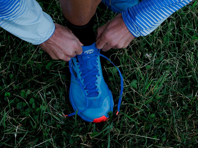 Gros plan sur des mains serrant les lacets d’une chaussure de trail sur l’herbe.