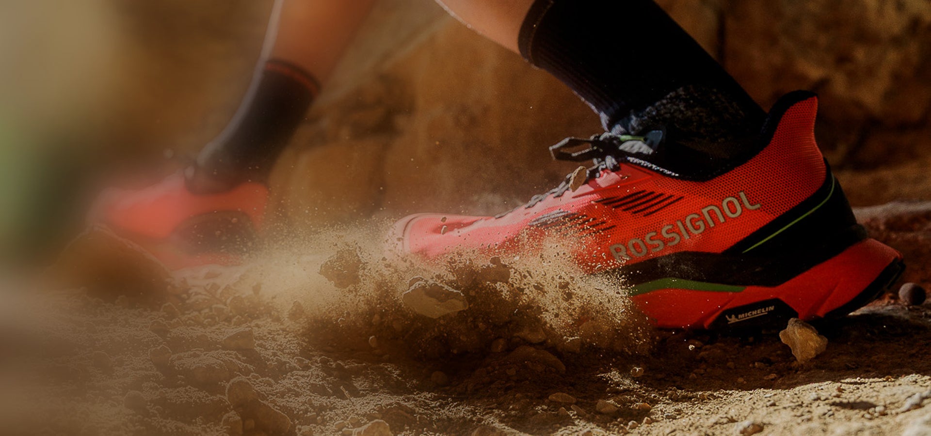 Gros plan sur une chaussure de trail rouge en action sur un sol sec et poussiéreux, projetant de la terre lors de l’appui.