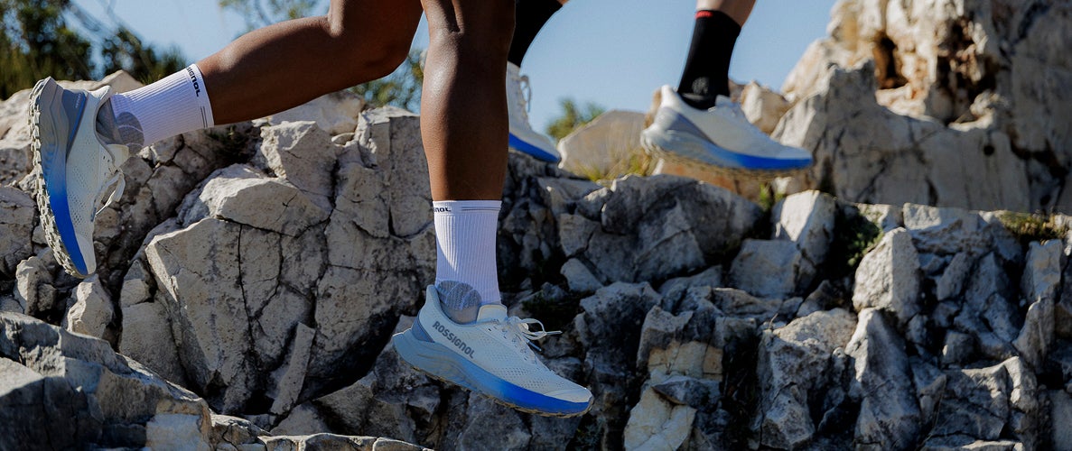Gros plan sur les jambes de deux personnes courant sur un terrain rocheux en montagne, avec des chaussures de trail en mouvement.