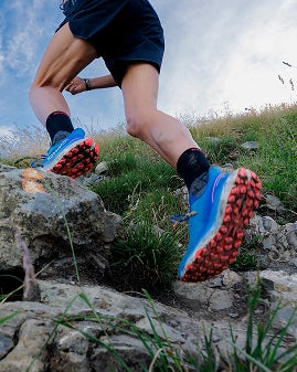 Une personne court sur un sentier rocheux en montagne, vue rapprochée sur les chaussures.