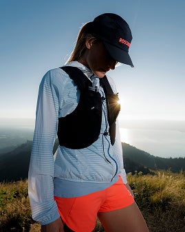 Une personne marche sur un sentier de montagne, avec un paysage vallonné au lever ou au coucher du soleil.