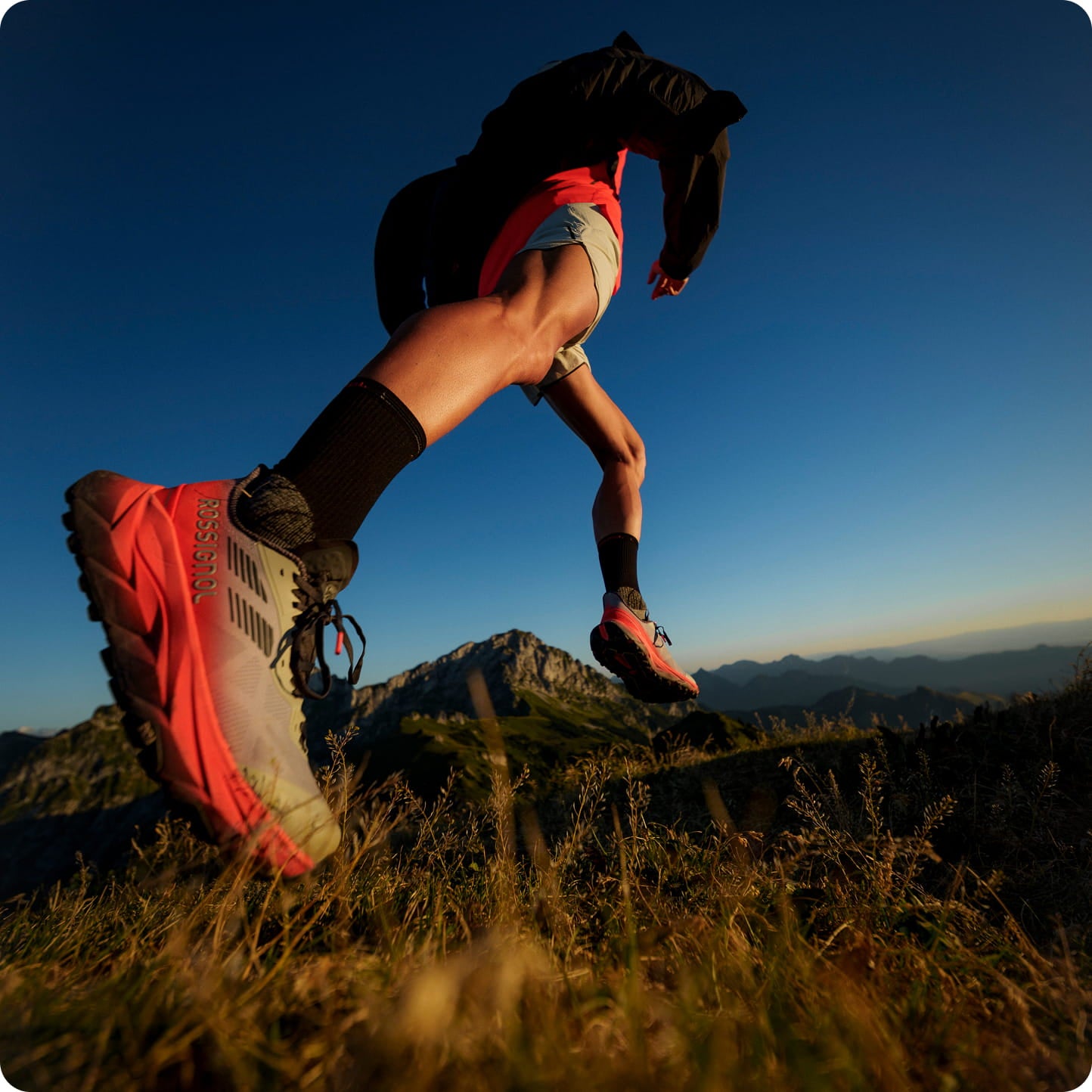 Red Vercors trail running shoe in motion during a dynamic uphill run on a grassy mountain path.