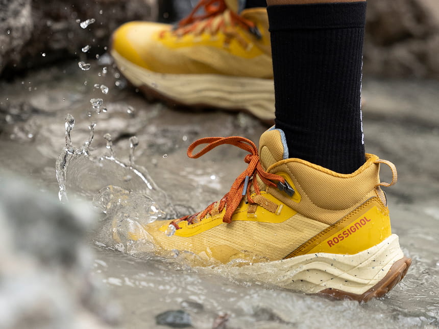 Focus sur les chaussures de randonnée Rossignol Altiridge imperméables. Il s'agit du modèle couleur "moutarde" et la personne marche dans une flaque d'eau pour montrer la résistance à l'eau.