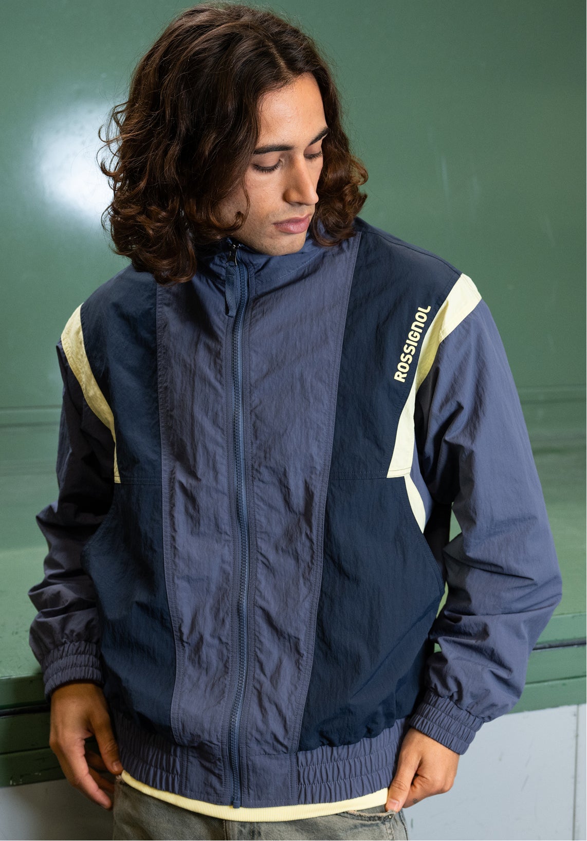 Close-up of a person wearing a blue and beige zip-up jacket with a Rossignol logo on the chest, in an indoor setting.