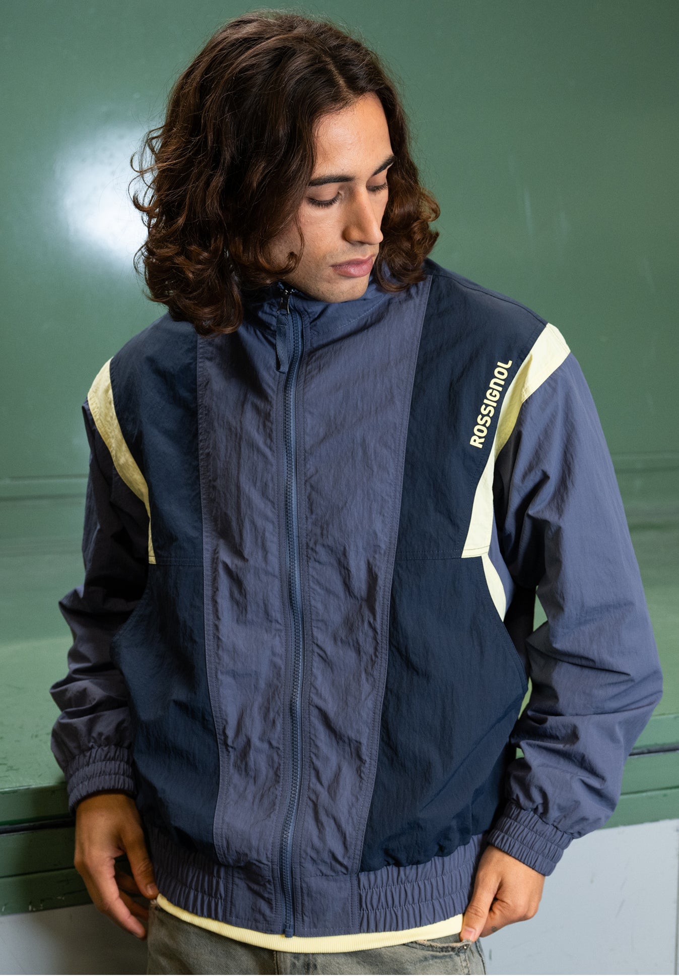 Close-up of a person wearing a blue and beige zip-up jacket with a Rossignol logo on the chest, in an indoor setting.