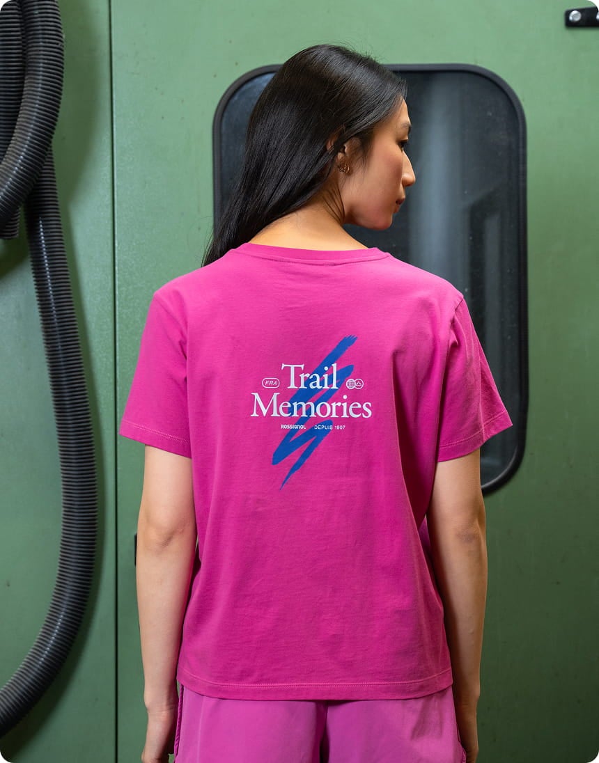 Rear view of a person wearing a pink T-shirt with a graphic design and printed text, in an industrial environment