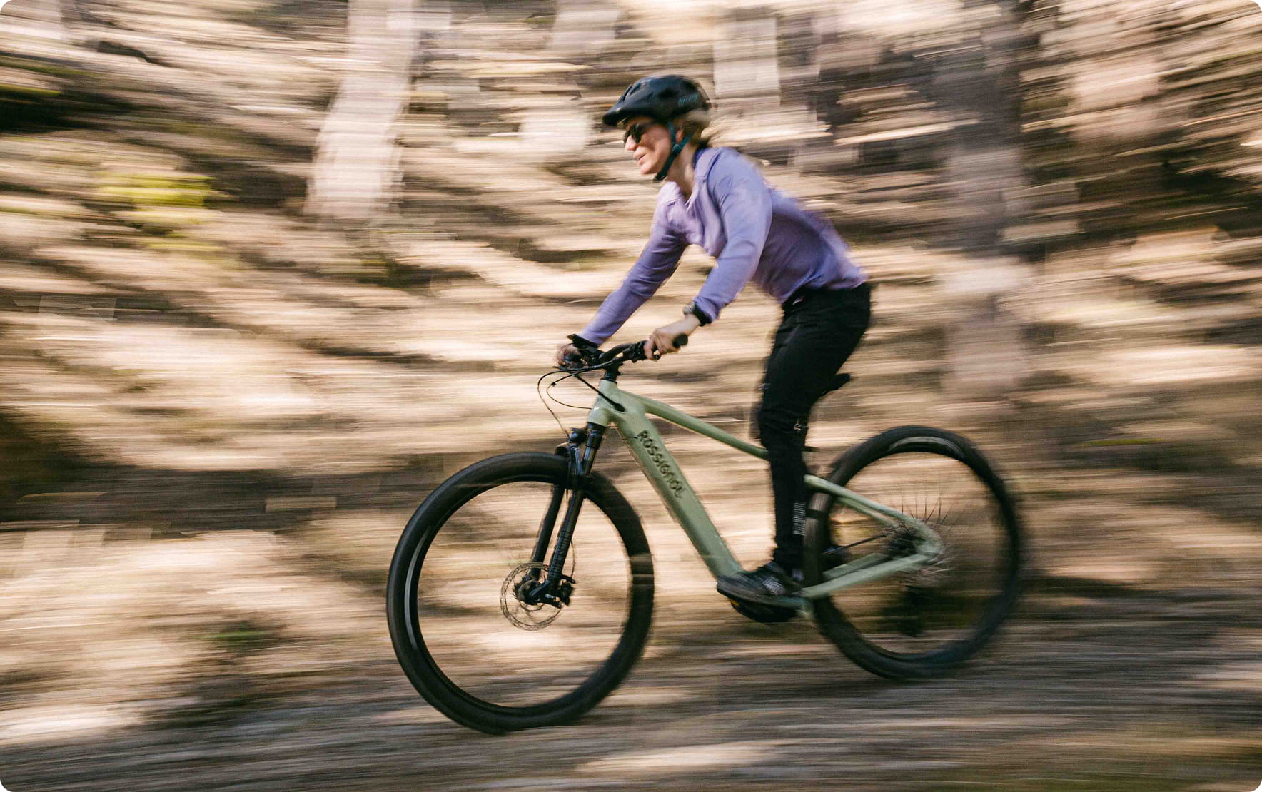 Ciclista su una mountain bike elettrica su un sentiero nel bosco con effetto di movimento.