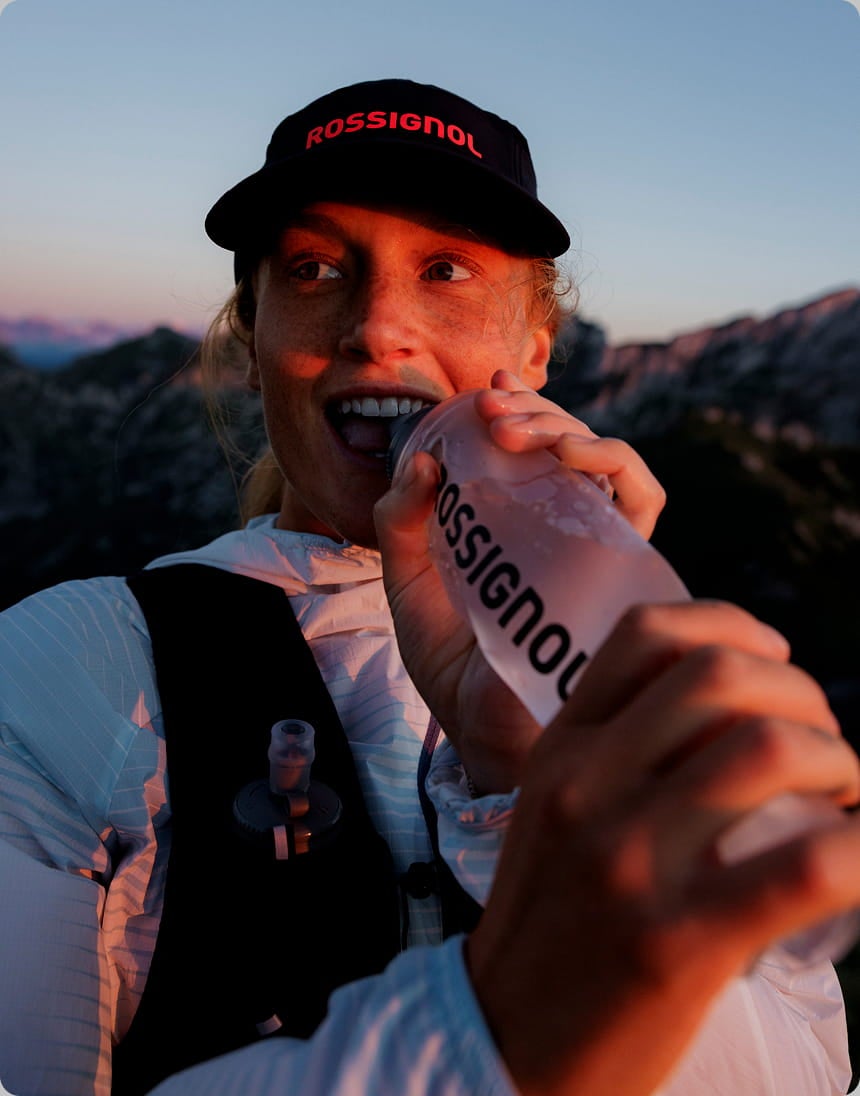 Atleta all’aperto che tiene una borraccia morbida Rossignol durante il trail running, con paesaggio montano.