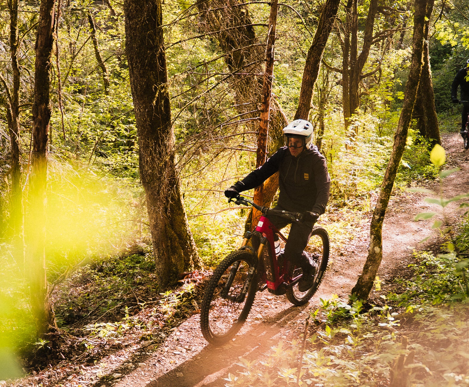 Rider on a Rossignol electric mountain bike riding along a narrow forest trail, surrounded by trees and vegetation on a winding dirt path.