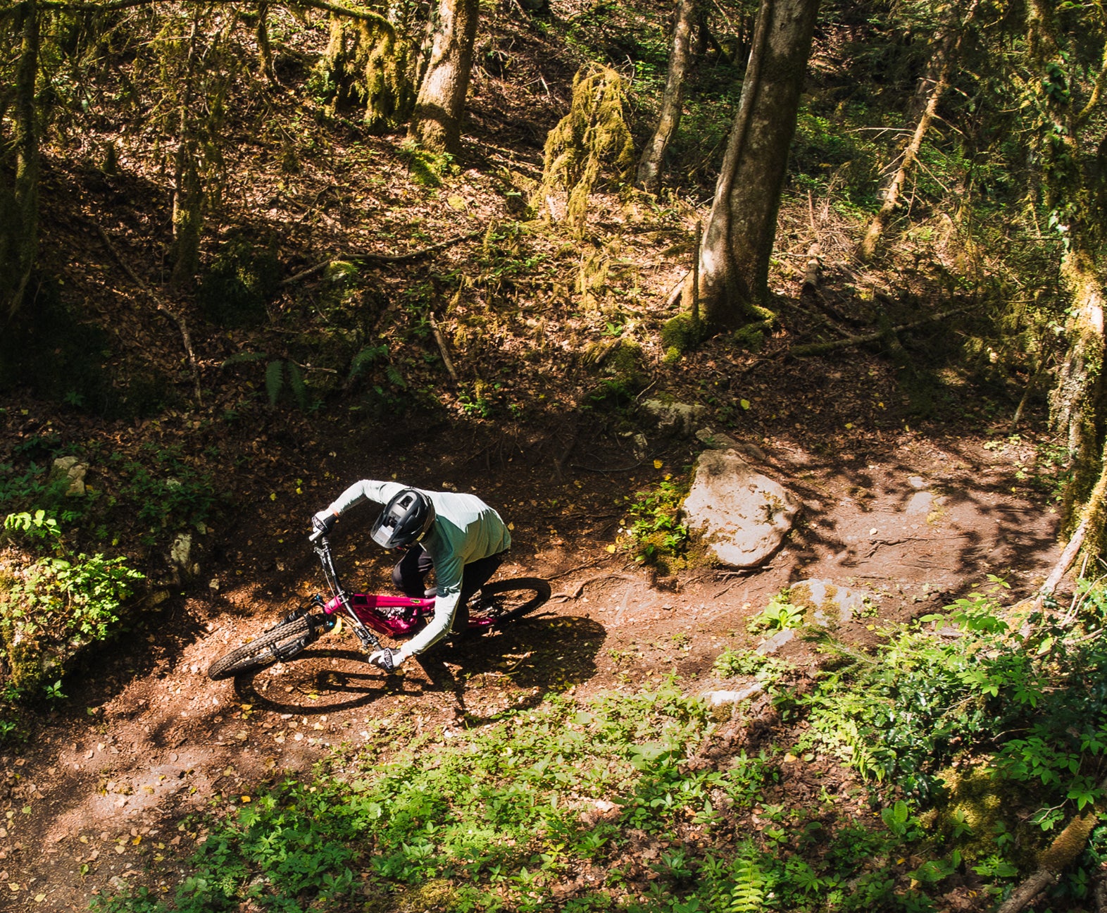 Top-down view of a rider on a Rossignol electric mountain bike taking a sharp turn on a dirt trail in a lush forest.