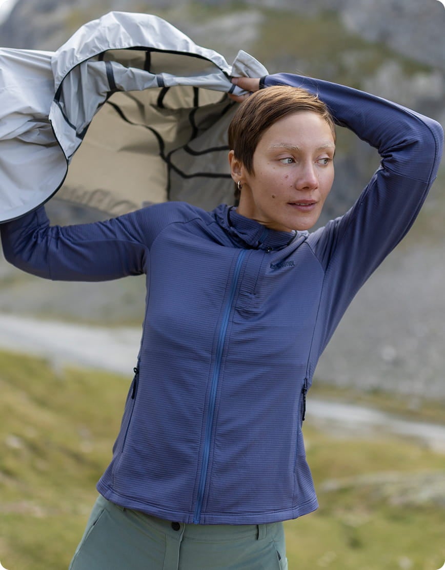 Frau im Freien mit einer hellen Jacke über den Schultern in einer Berglandschaft.