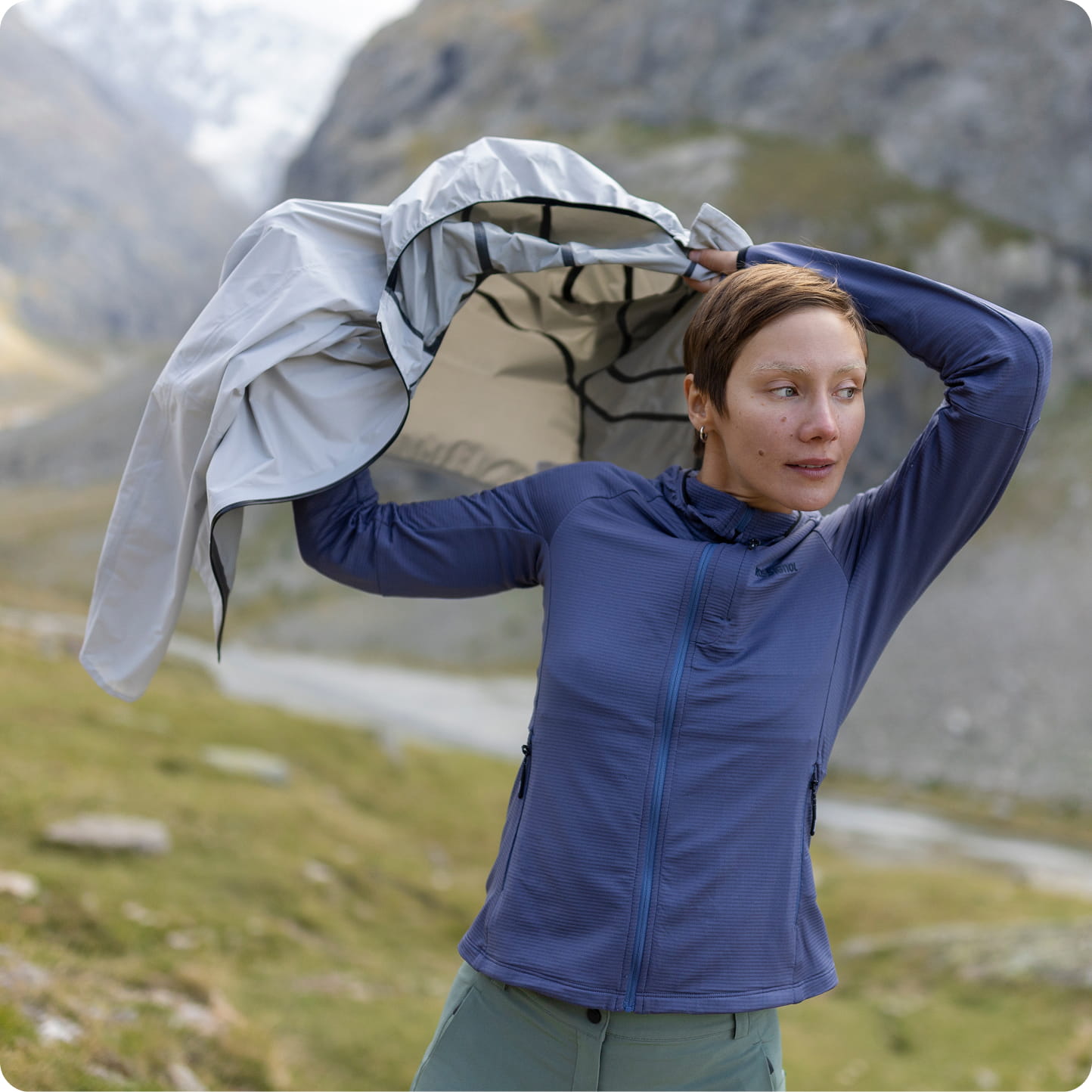 Frau im Freien mit einer hellen Jacke über den Schultern in einer Berglandschaft.