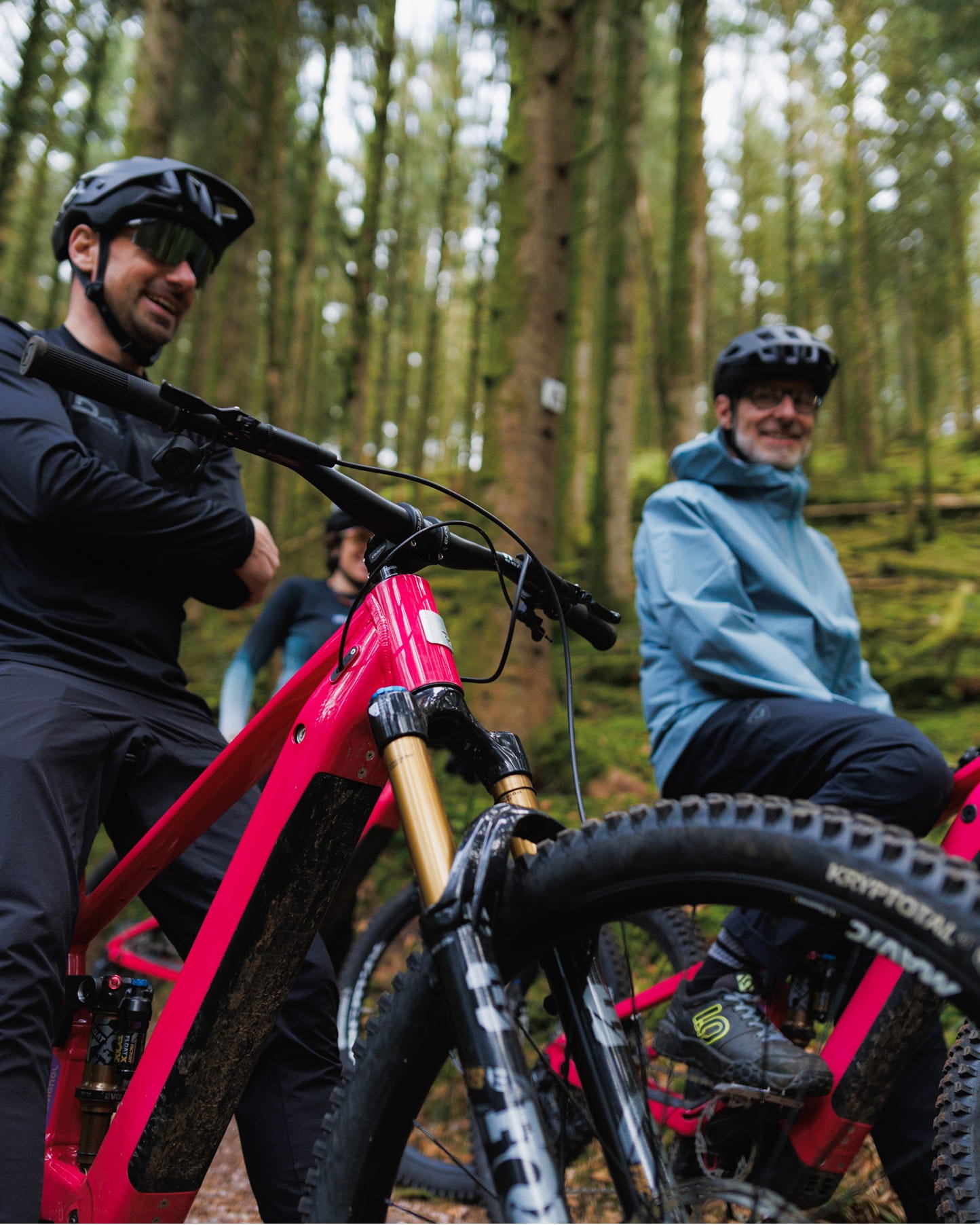 Two athletes, sitting on their Rossignol After Hours bikes. They are chatting during their mountain bike ride in the forest. One is wearing a black outfit and the other a light blue jacket.