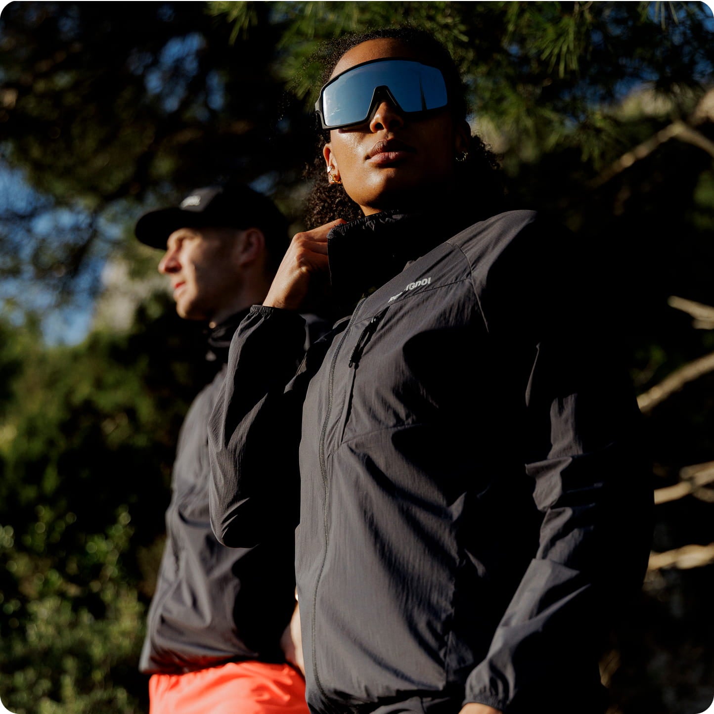 Deux personnes portant des vestes techniques de trail en extérieur, dont l'une avec des lunettes de sport à écran, dans un environnement montagneux.