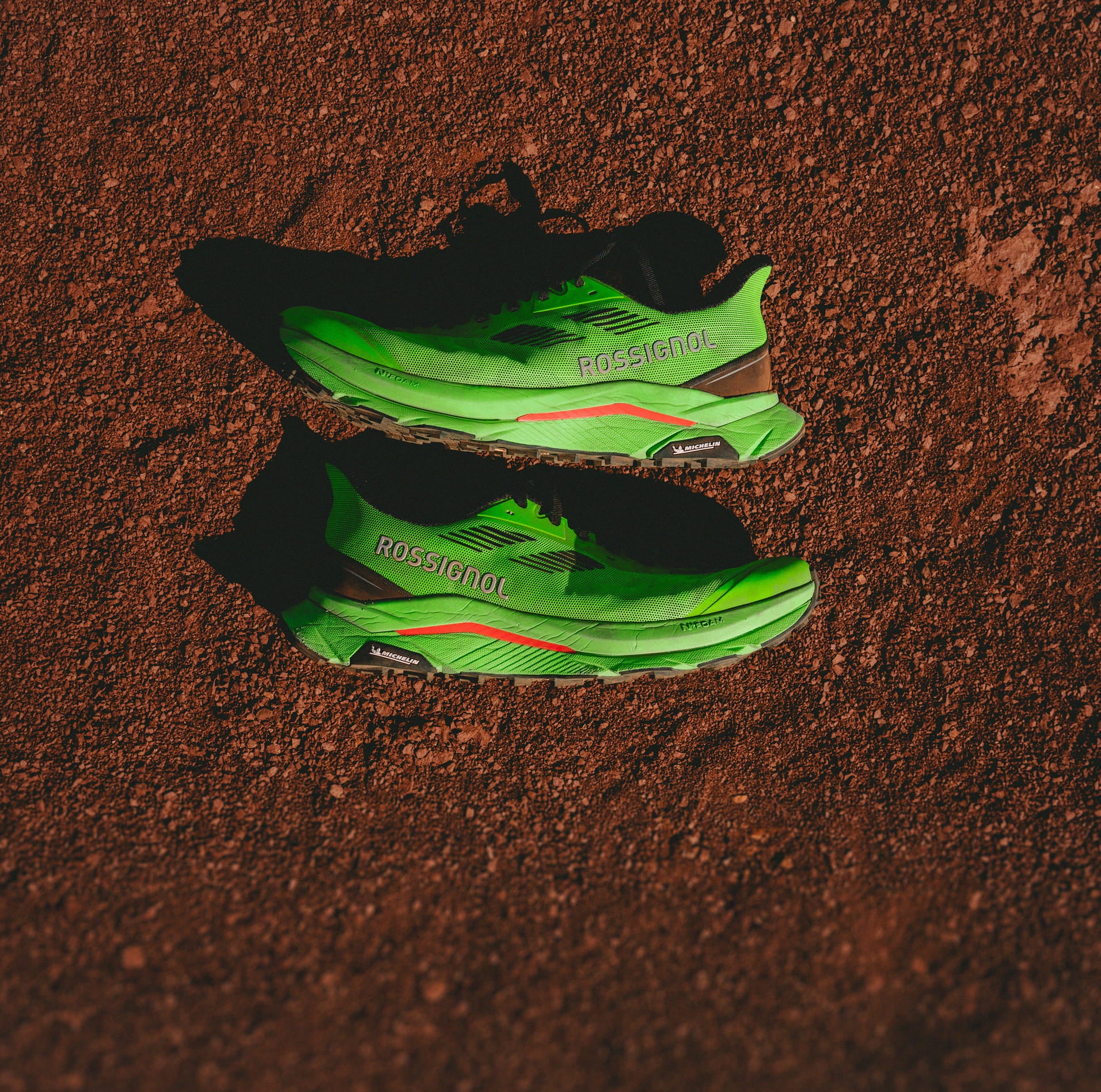 Top-down view of the limited edition "Super Project" Vezor trail shoes placed on dirt.