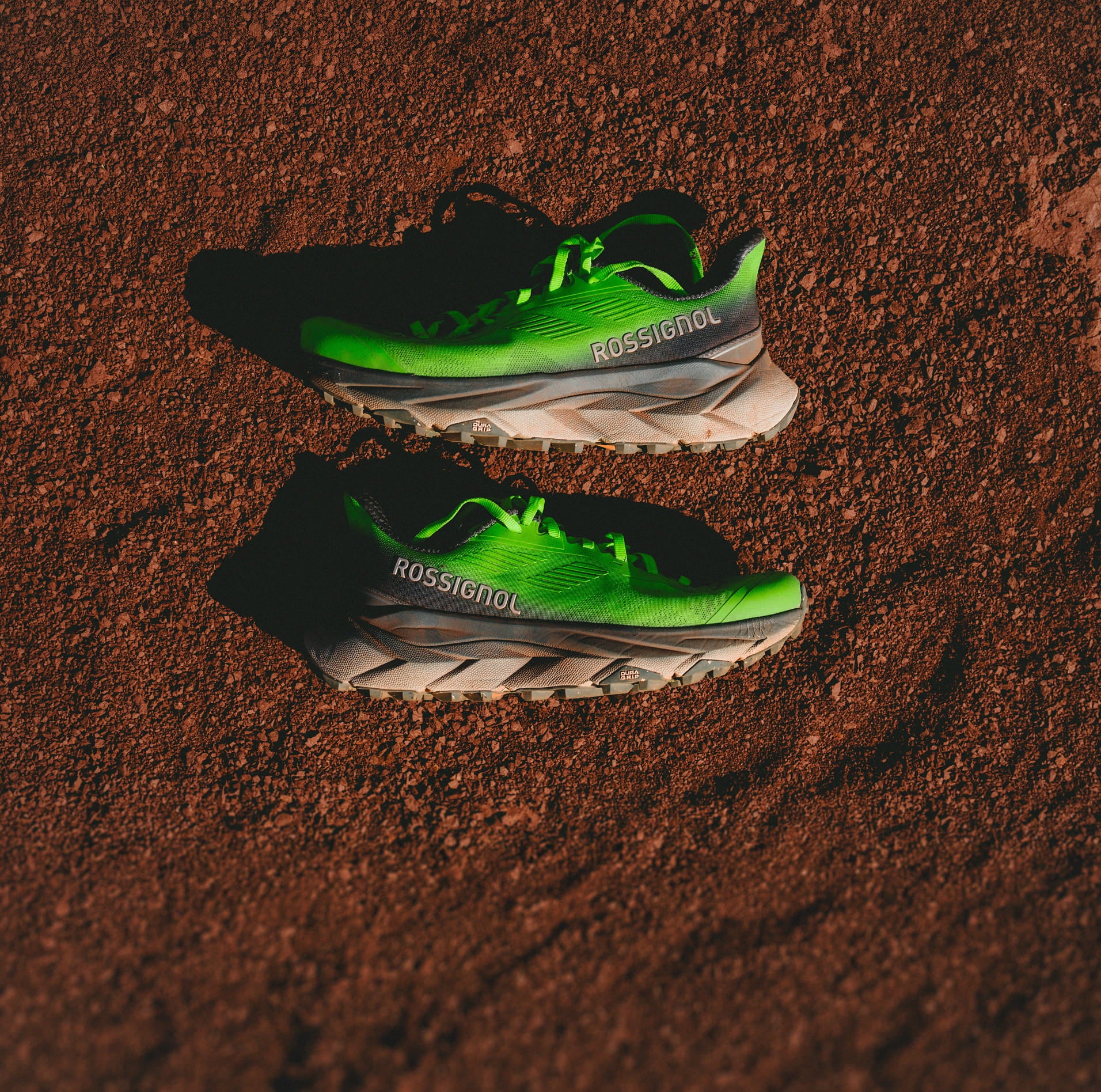 Top-down view of the limited edition "Super Project" Vercors trail shoes placed on dirt.