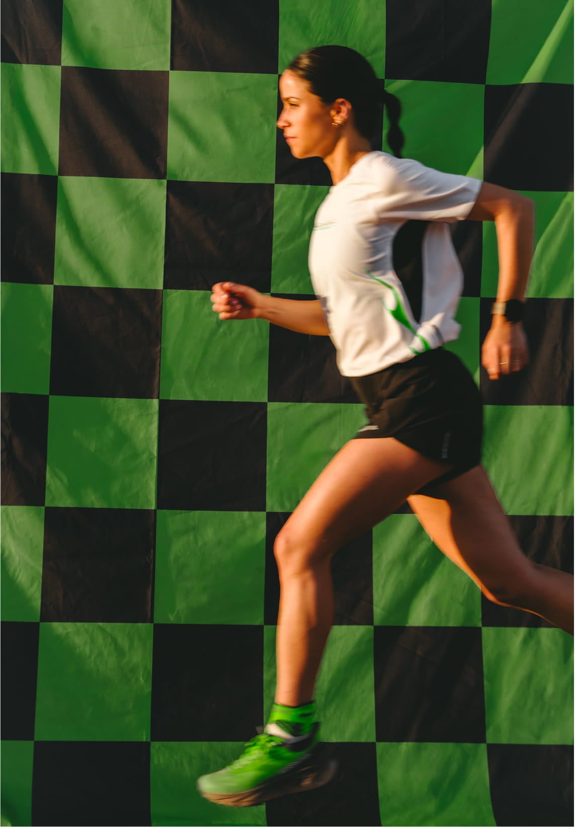 Female athlete running in profile against a black and green checkerboard background