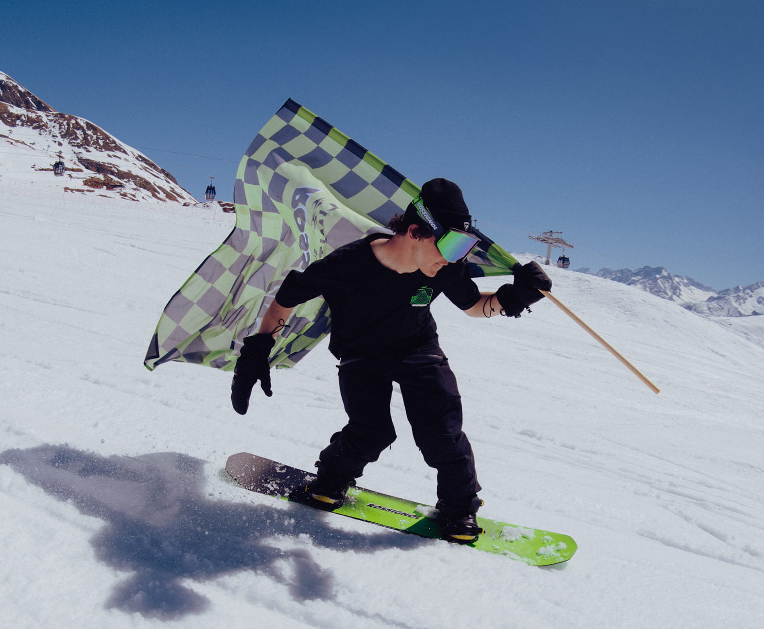 Snowboarder portant un drapeau à damier vert et noir sur les pistes