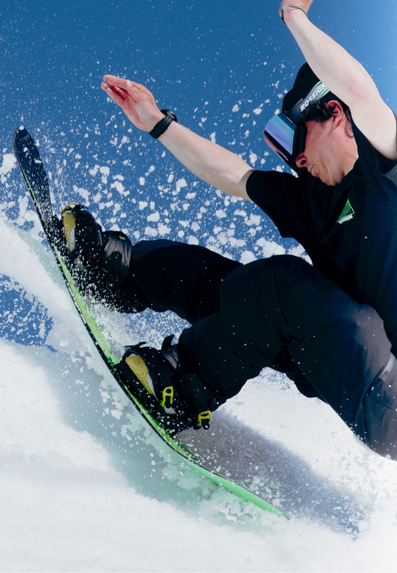 Snowboarder au sommet d’une butte enneigée projetant de la neige avec le snowboard REVENANT de Rossignol