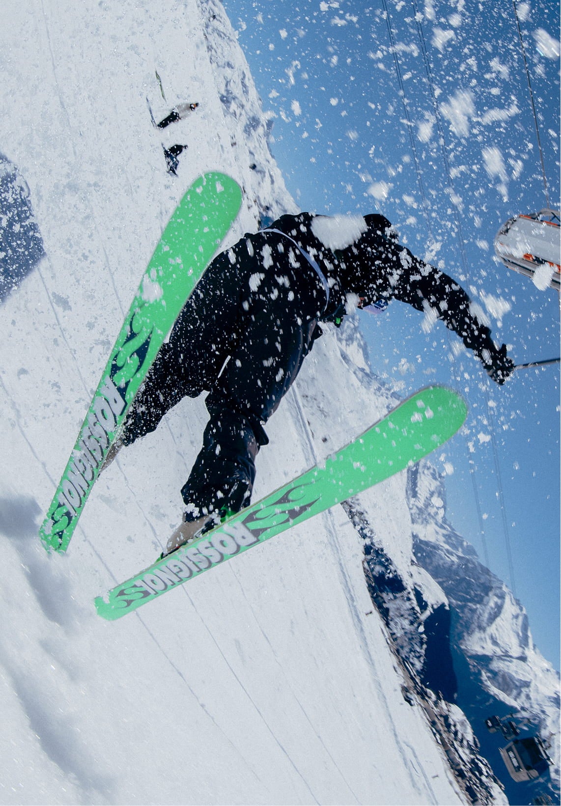 Skieur réalisant une figure dans la neige avec les skis SUPER BLACKOPS de Rossignol, montrant les semelles en projetant de la neige