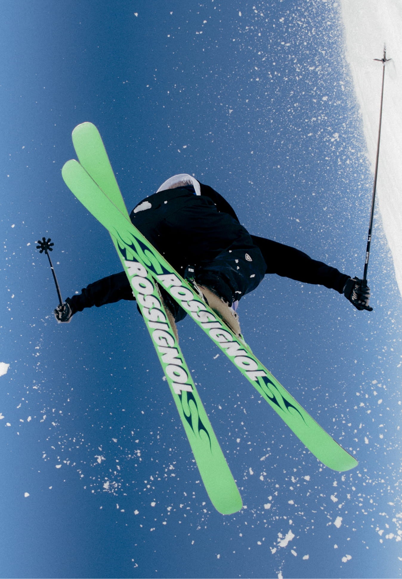 Vue du dessous d’un athlète en plein saut avec les skis SUPER BLACKOPS de Rossignol croisés en l’air