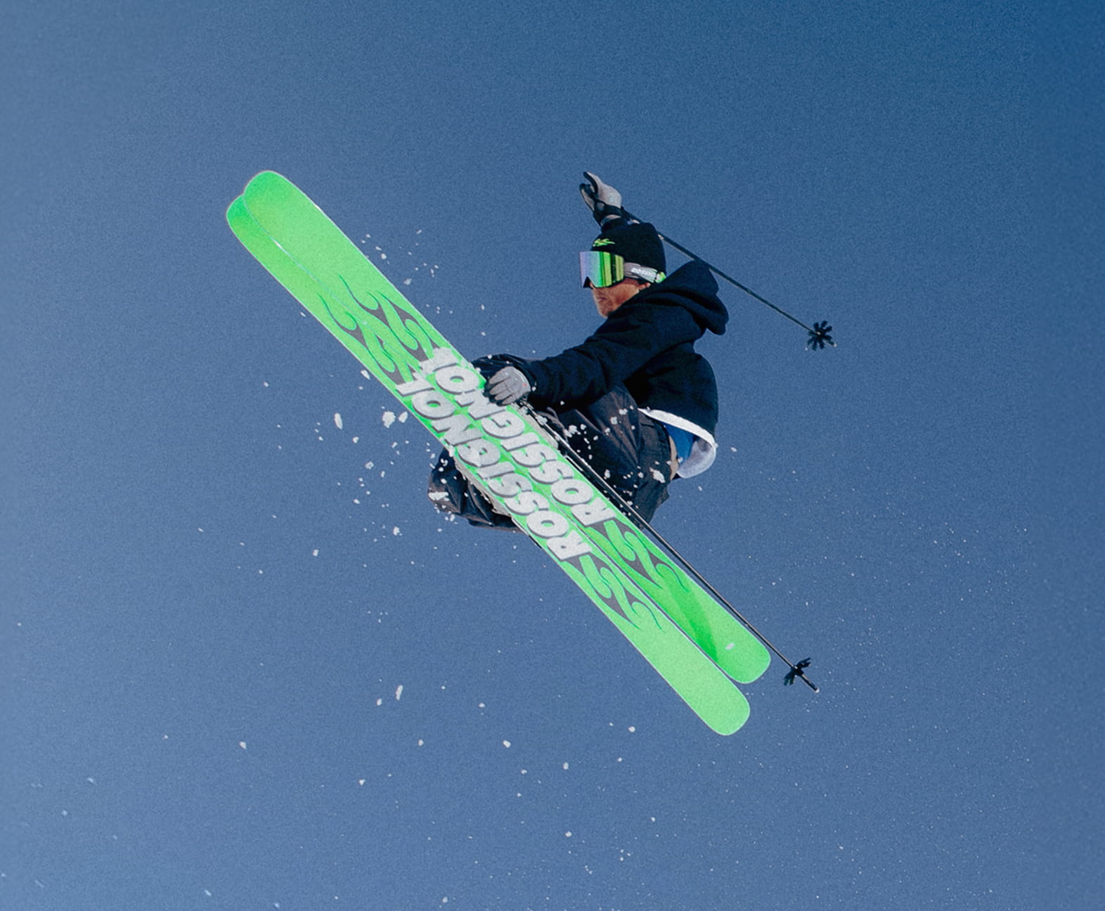 Skieur en plein saut avec les skis SUPER BLACKOPS de Rossignol, une main sur les skis et l’autre en l’air