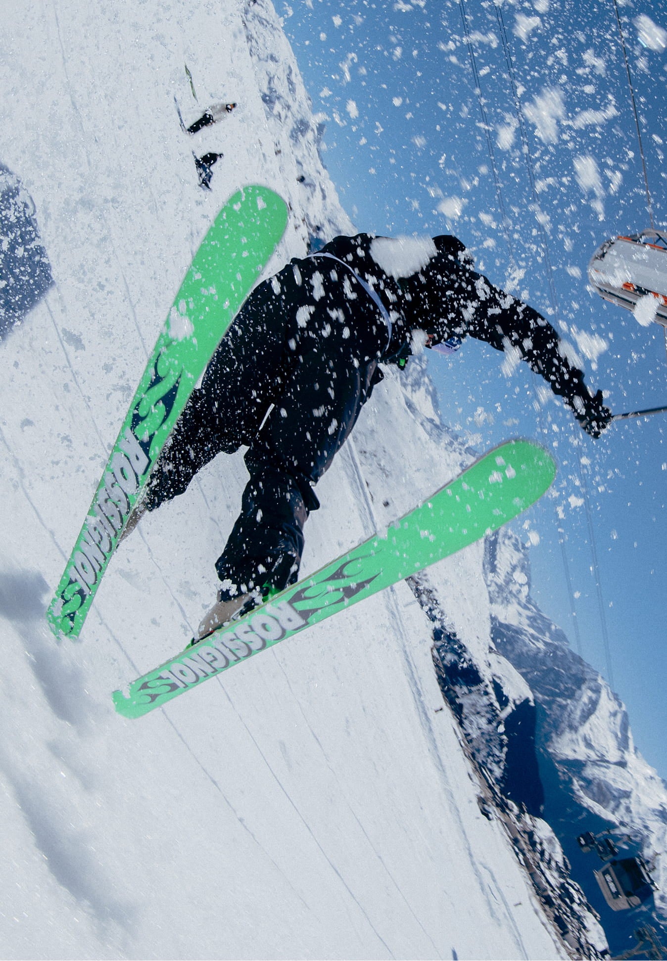 Skieur réalisant une figure dans la neige avec les skis SUPER BLACKOPS de Rossignol, montrant les semelles en projetant de la neige