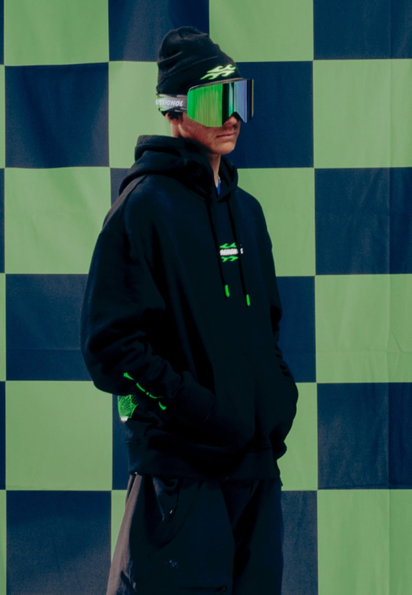 Athlete wearing the Rossignol SUPER PROJECT HOODIE in front of a green and black checkerboard background