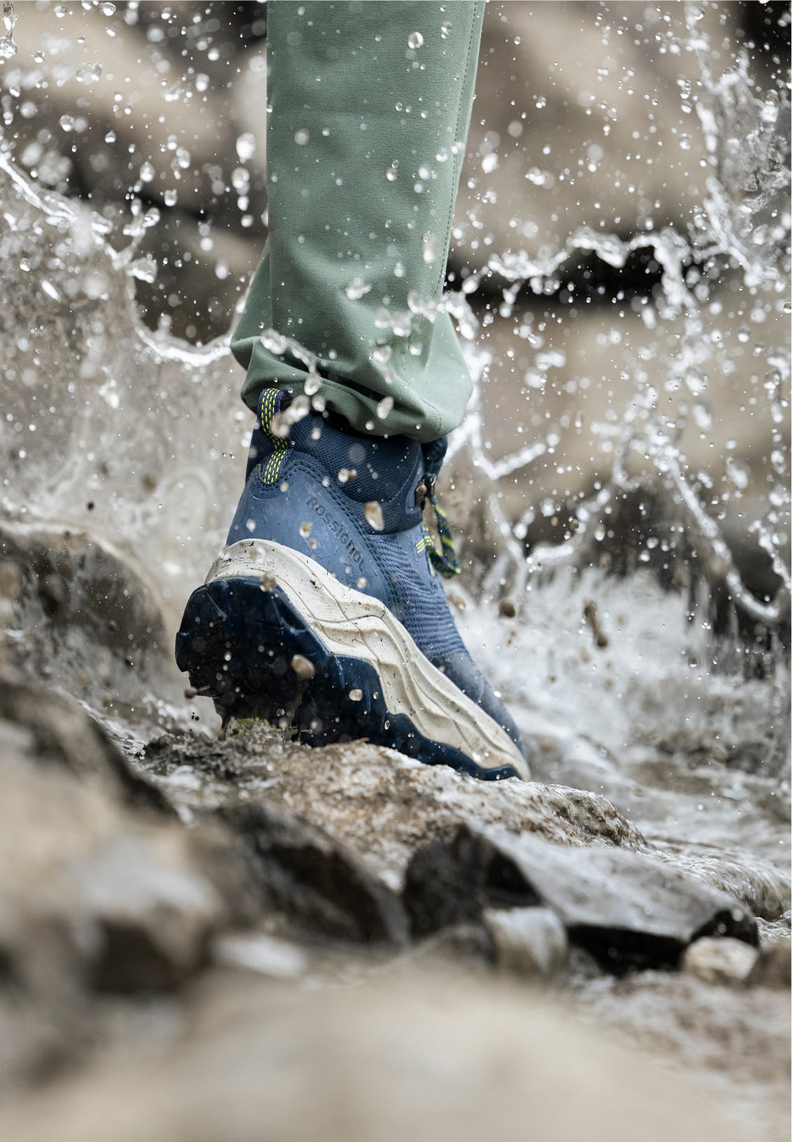 Close-up of the Rossignol ALTIRIDGE MID WP navy hiking boot stepping on a rock in a river with splashing water