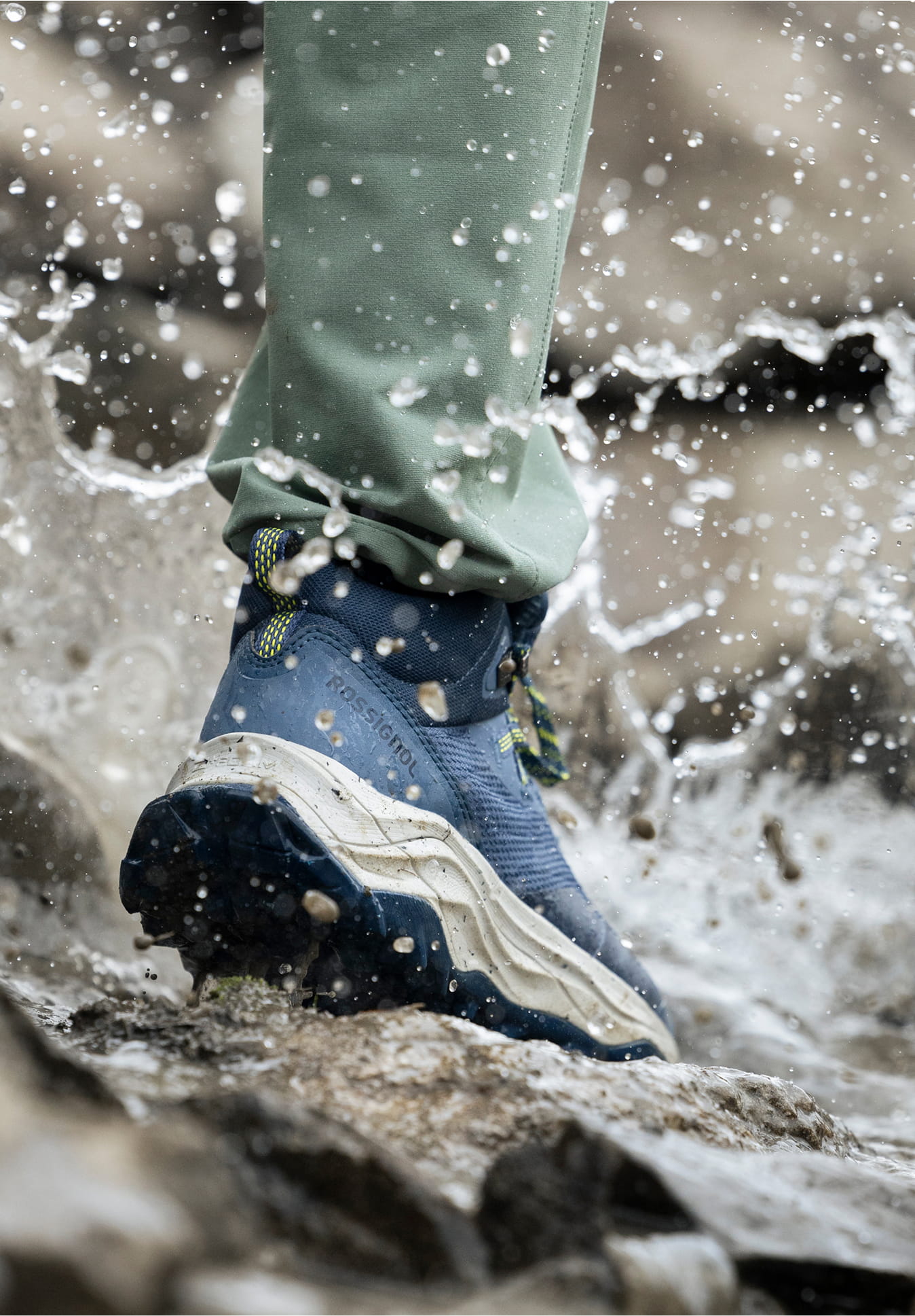 Close-up of the Rossignol ALTIRIDGE MID WP navy hiking boot stepping on a rock in a river with splashing water
