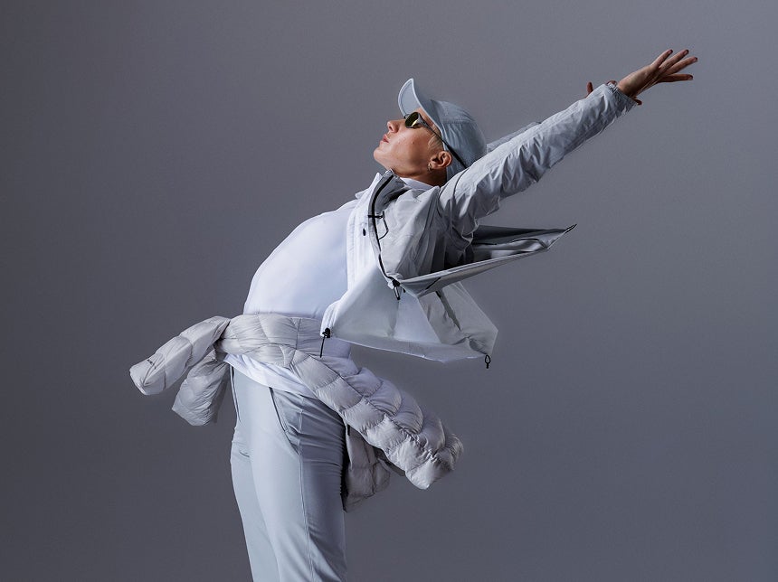 Person in einer weißen Rossignol Bekleidung in einer dynamischen Pose vor einem Studiohintergrund.