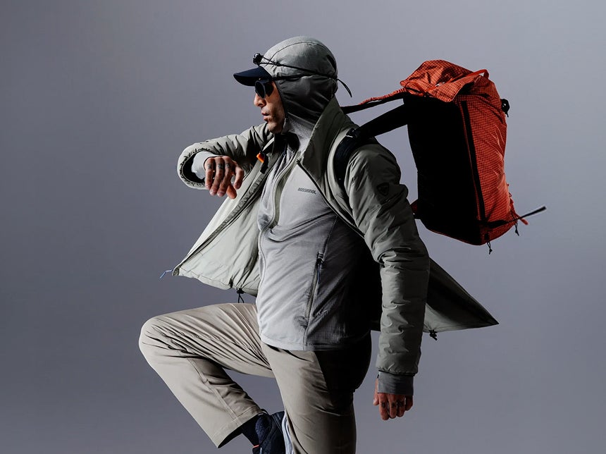 Person mit Rossignol Outdoor-Bekleidung und Rucksack in einer dynamischen Pose vor einem Studiohintergrund.