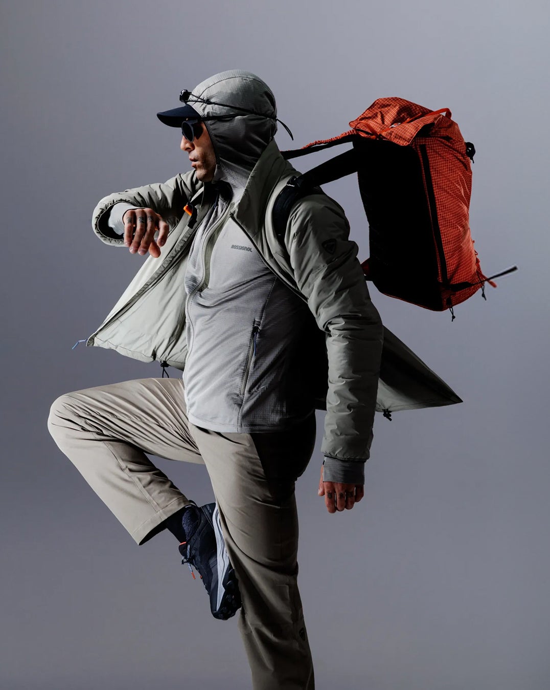 Person mit Rossignol Outdoor-Bekleidung und Rucksack in einer dynamischen Pose vor einem Studiohintergrund.