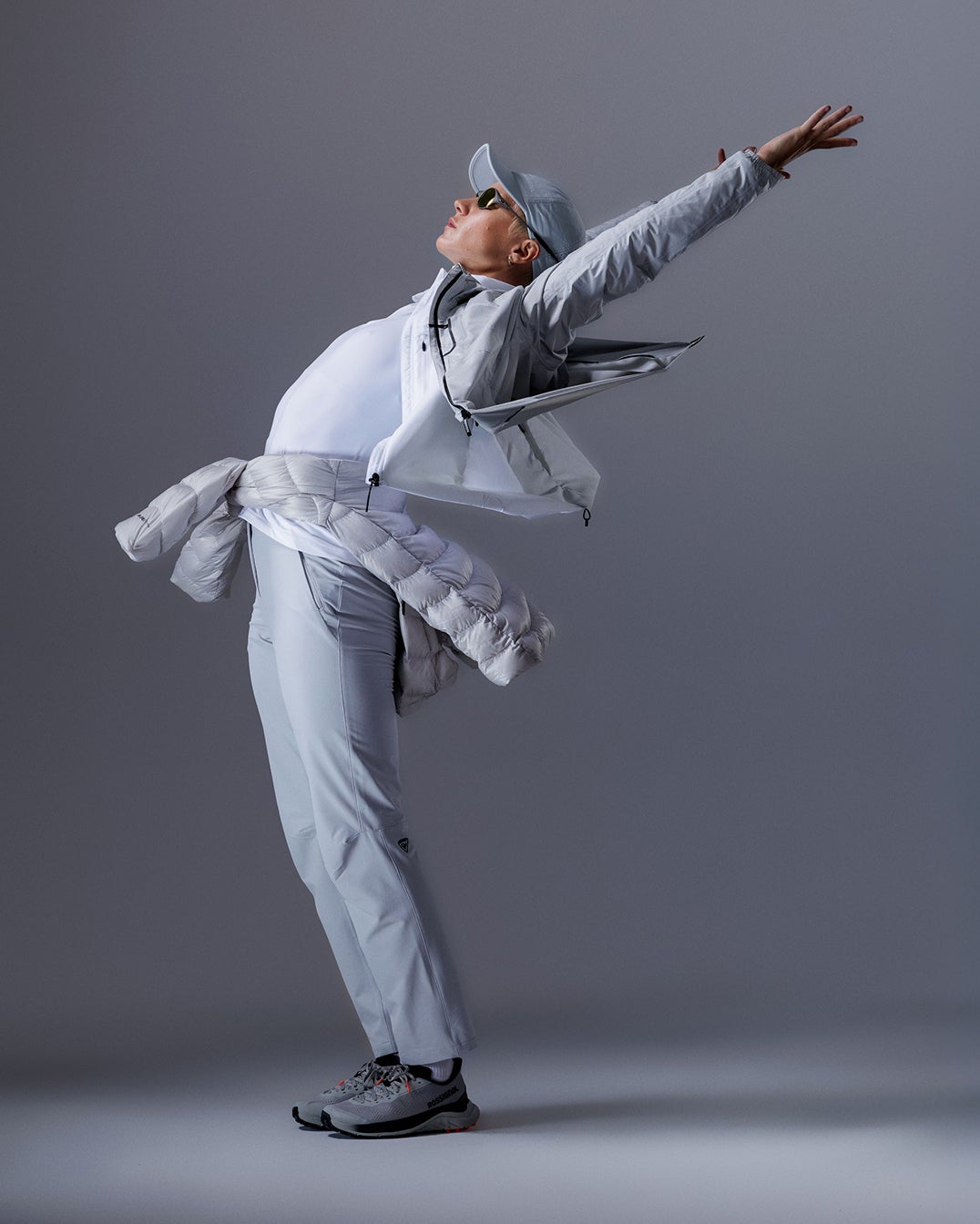 Person in einer weißen Rossignol Bekleidung in einer dynamischen Pose vor einem Studiohintergrund.