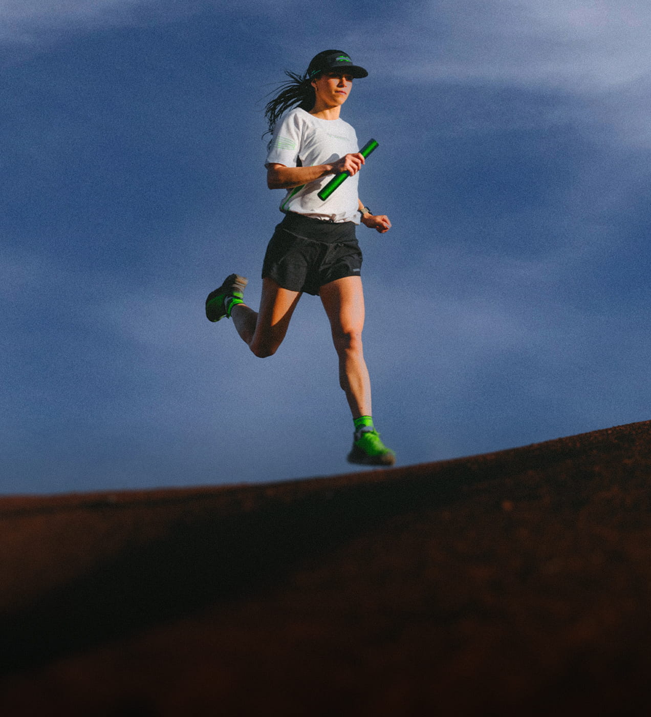 Trail runner equipped with performance apparel running along a ridge beneath a cloudy sky, showcasing the trail running capsule.