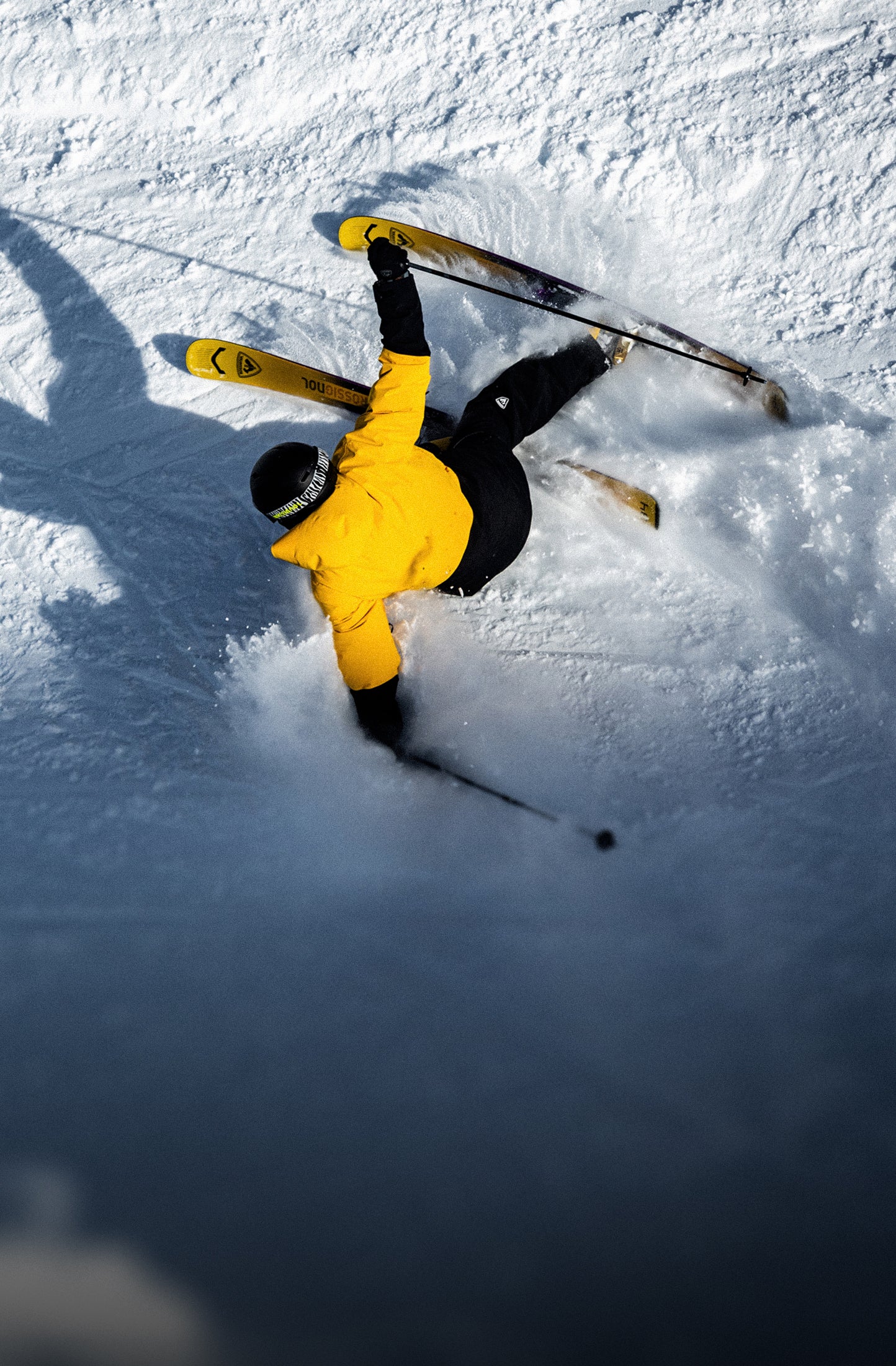 Skieur vu de dessus effectuant un virage dans la neige sur une piste enneigée, portant une veste jaune.