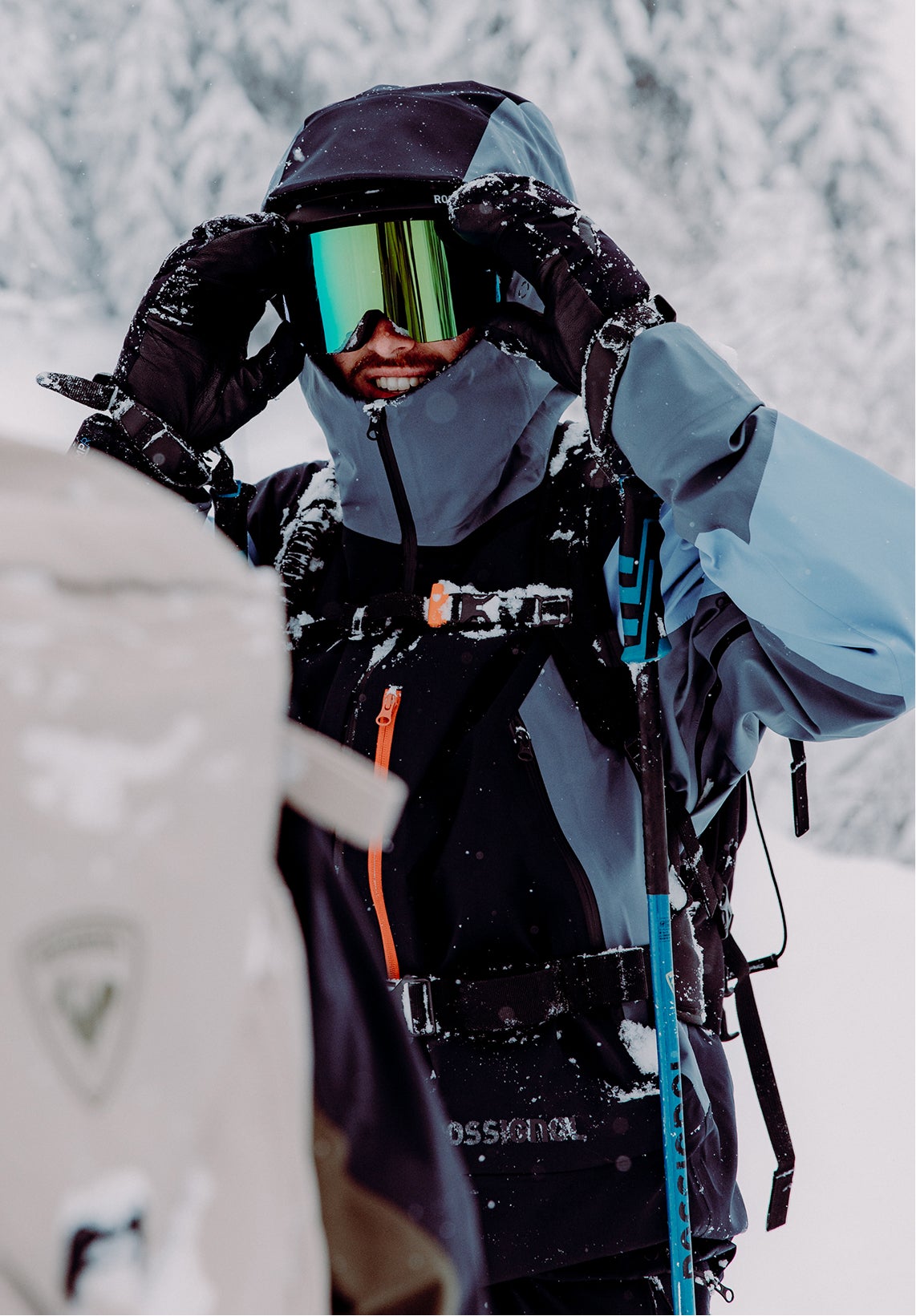 A smiling freeride skier on a cloudy day, wearing a Rossignol Proclivity ski outfit and goggles with a holographic lens.