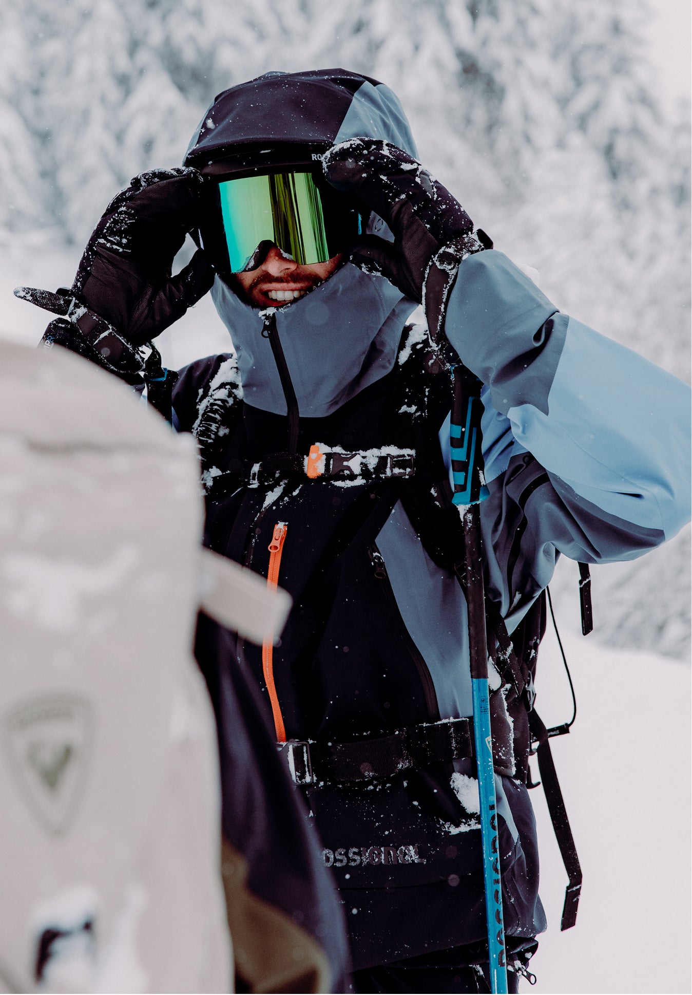A smiling freeride skier on a cloudy day, wearing a Rossignol Proclivity ski outfit and goggles with a holographic lens.