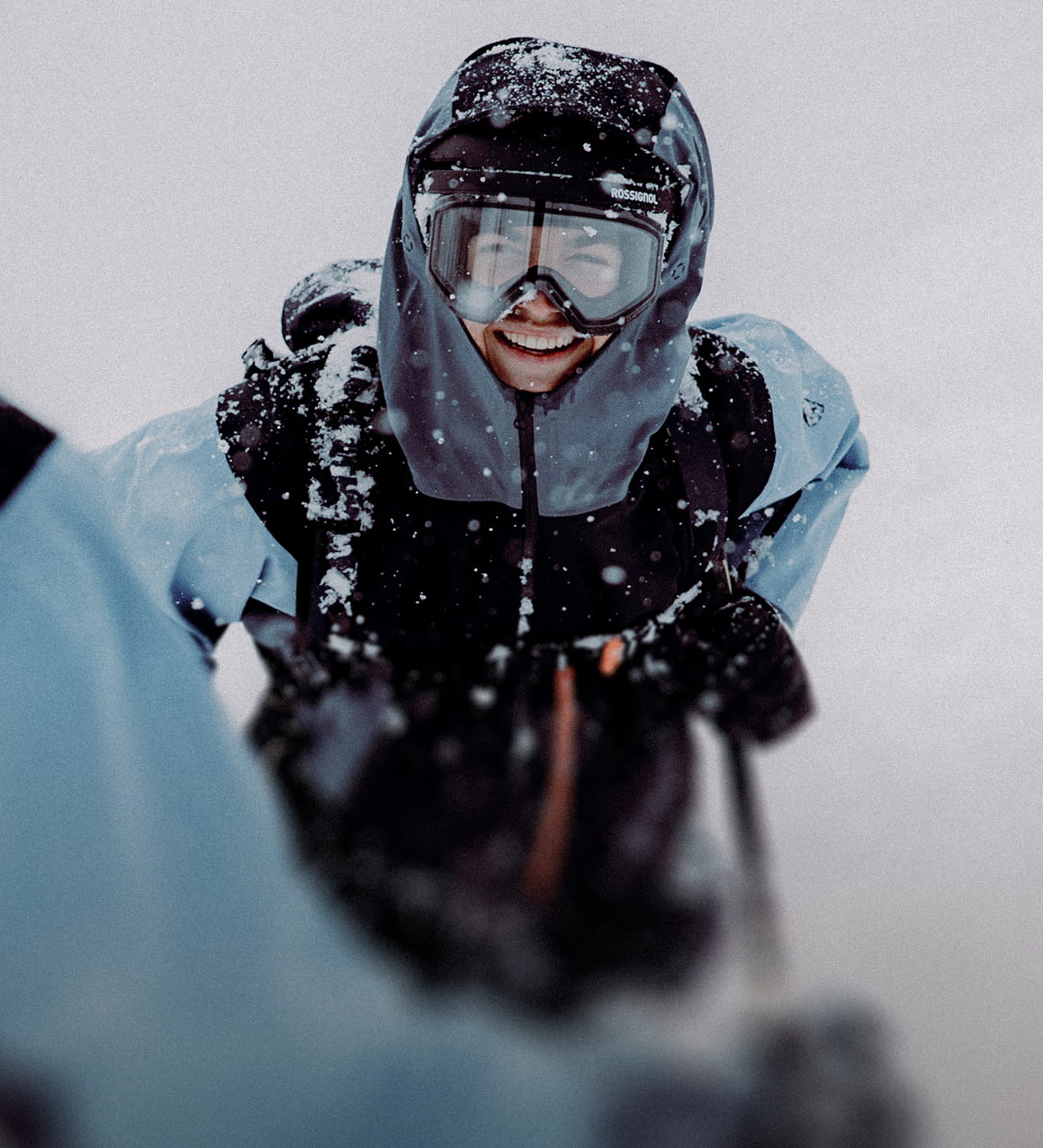 A smiling freeride skier on a cloudy day, wearing a Rossignol Proclivity ski outfit and a clear visor goggle.