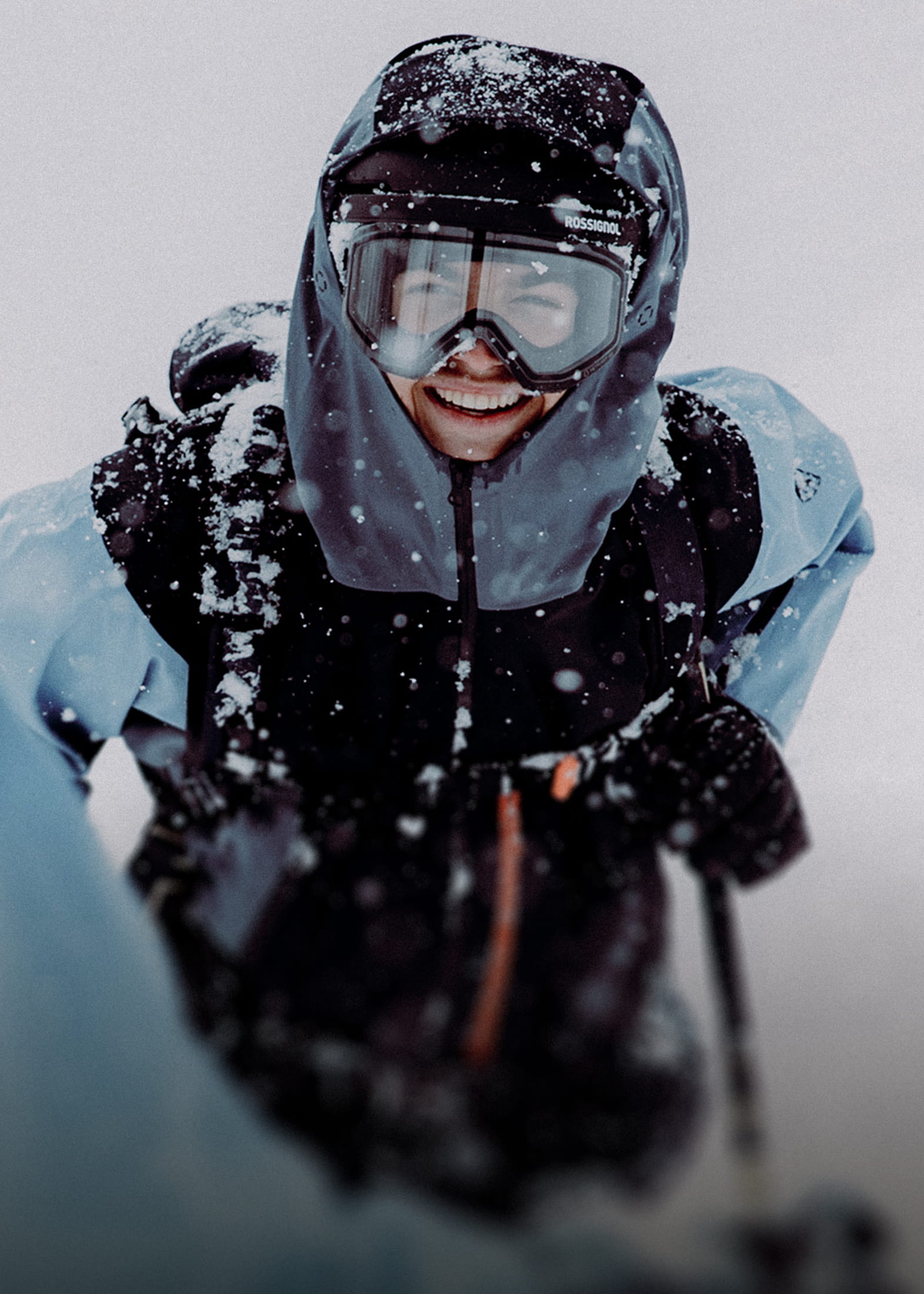 A smiling freeride skier on a cloudy day, wearing a Rossignol Proclivity ski outfit and a clear visor goggle.