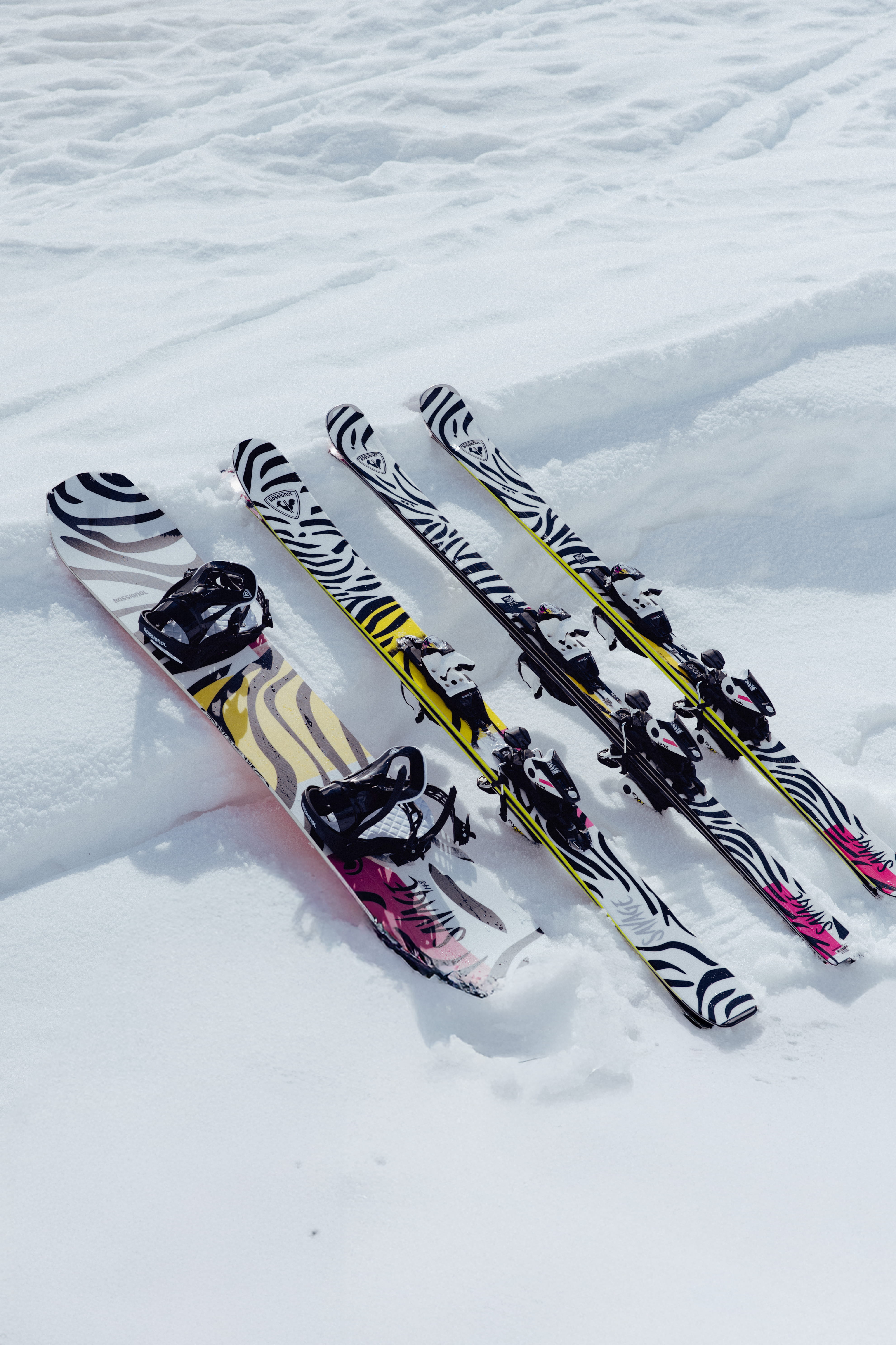 A snowboard and three skis with matching black-and-white graphic designs resting on the snow.